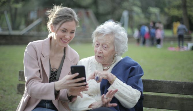 En ung kvinne og en gammel kvinne som ser på en telefon på benken