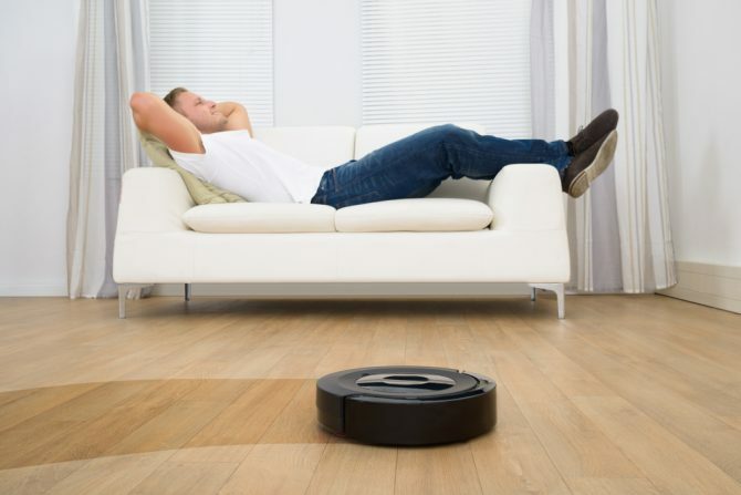 Mann som slapper av på sofaen med robotstøvsuger på tregulv