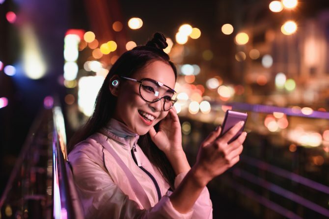 glad asiatisk jente som har videochat ved hjelp av smarttelefon og i ørehodetelefoner