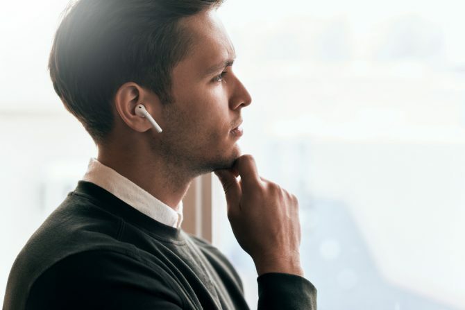 Mann tenker mens han ser ut av vinduet iført trådløse i øretelefoner